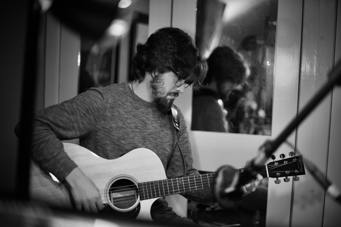 Black and white photo of Brigham Cason tracking acoustic guitar in a recording studio